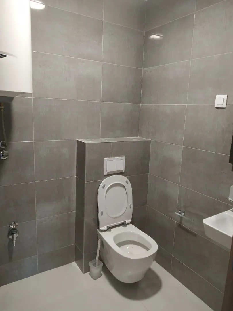 Moderno kupatilo sa sivim pločicama i ugradnim vodokotlićem.