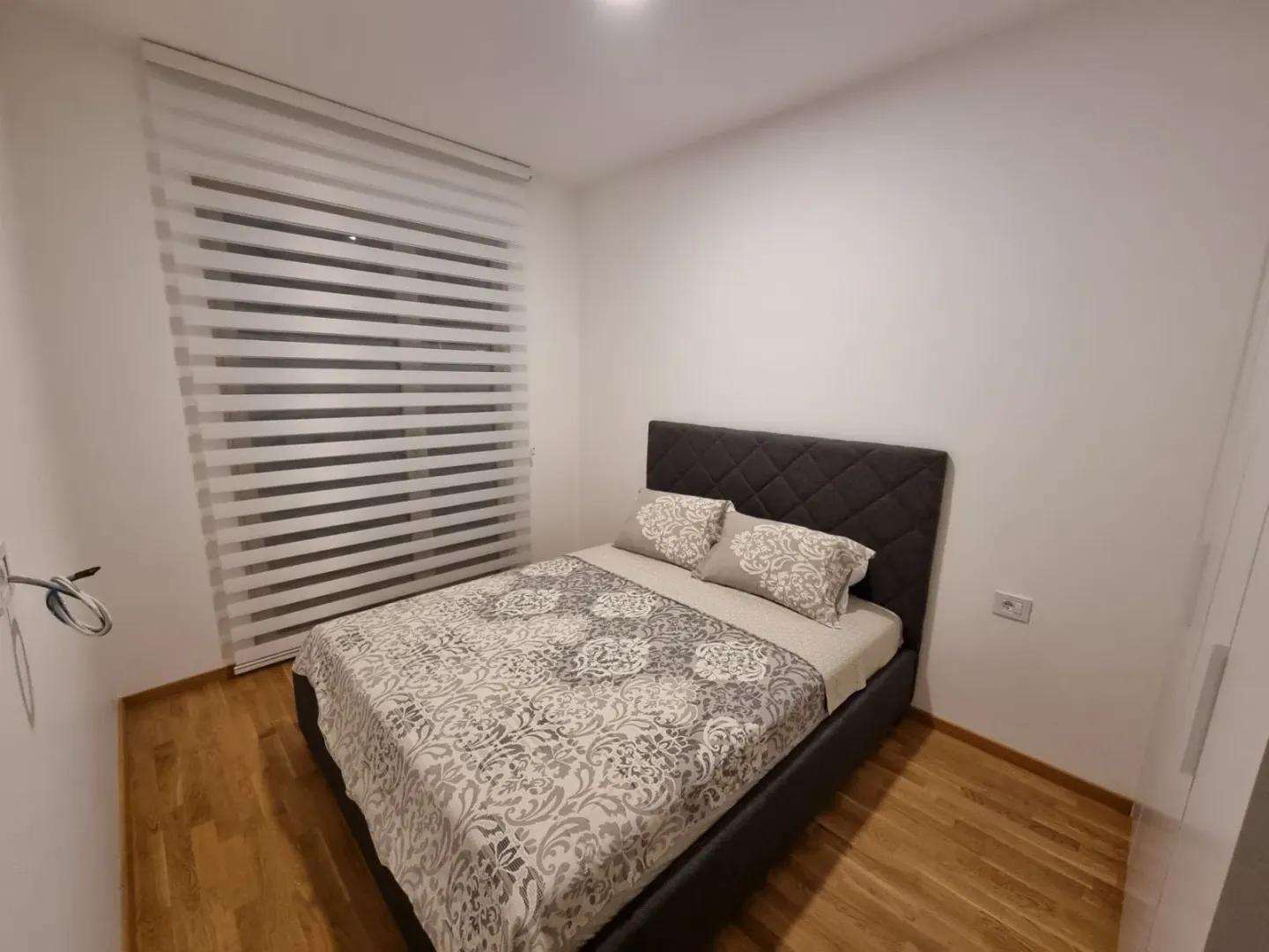 A bedroom with a double bed and a window with blinds.