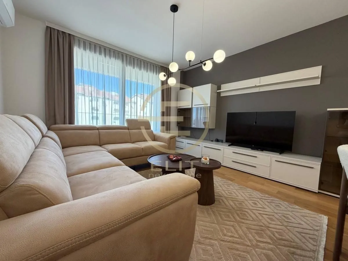 Udobna dnevna soba sa velikom ugaonom garniturom, TV komodom i modernim lusterom.
