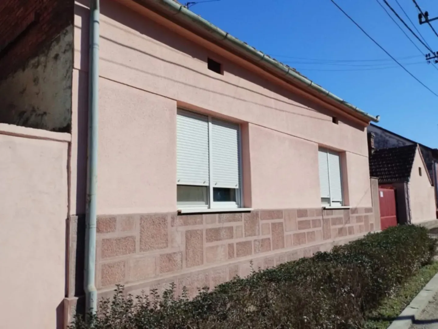Pogled na spoljašnjost kuće sa ružičastom fasadom.