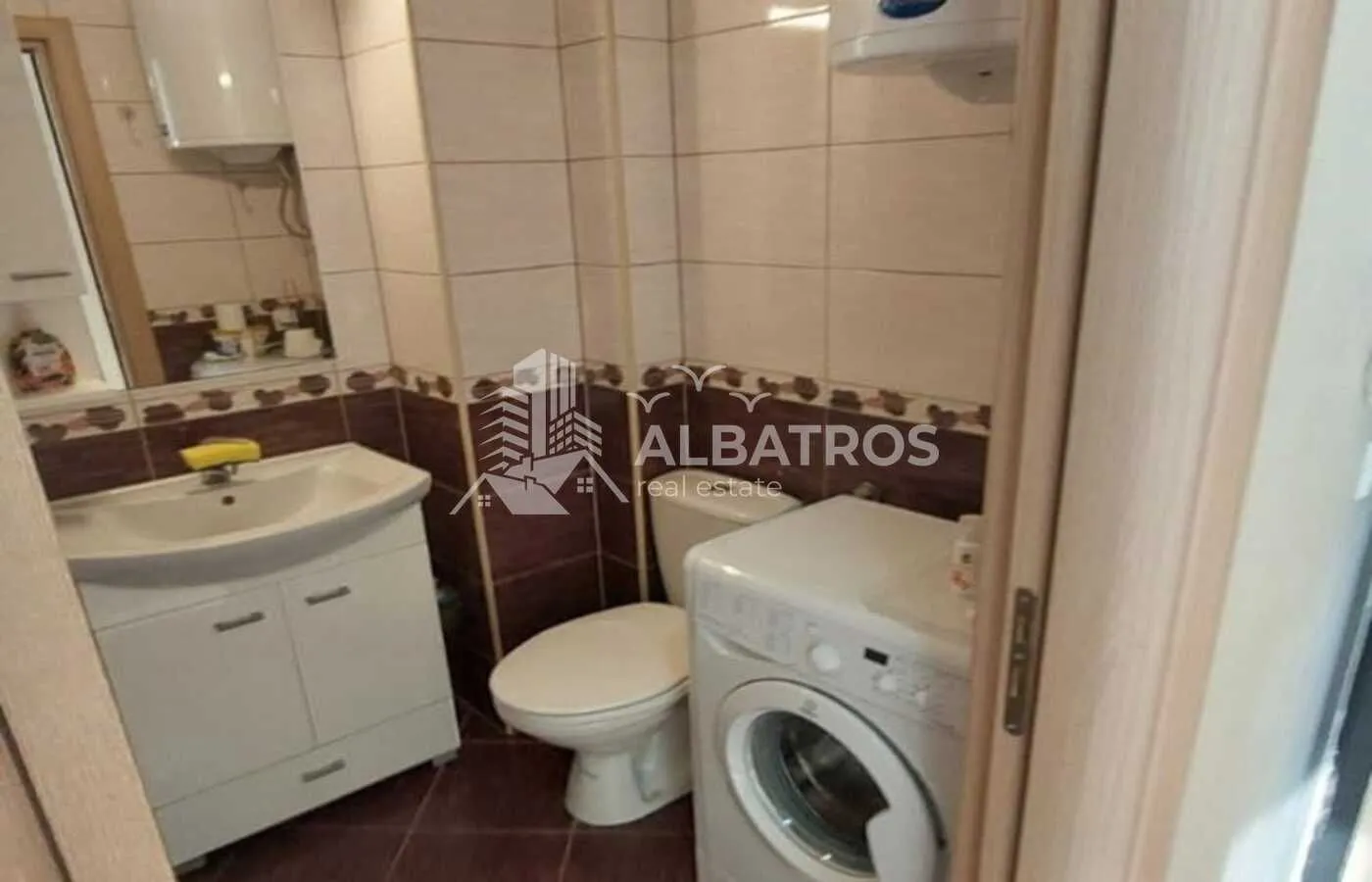 Small tiled bathroom equipped with a sink, toilet, and washing machine.