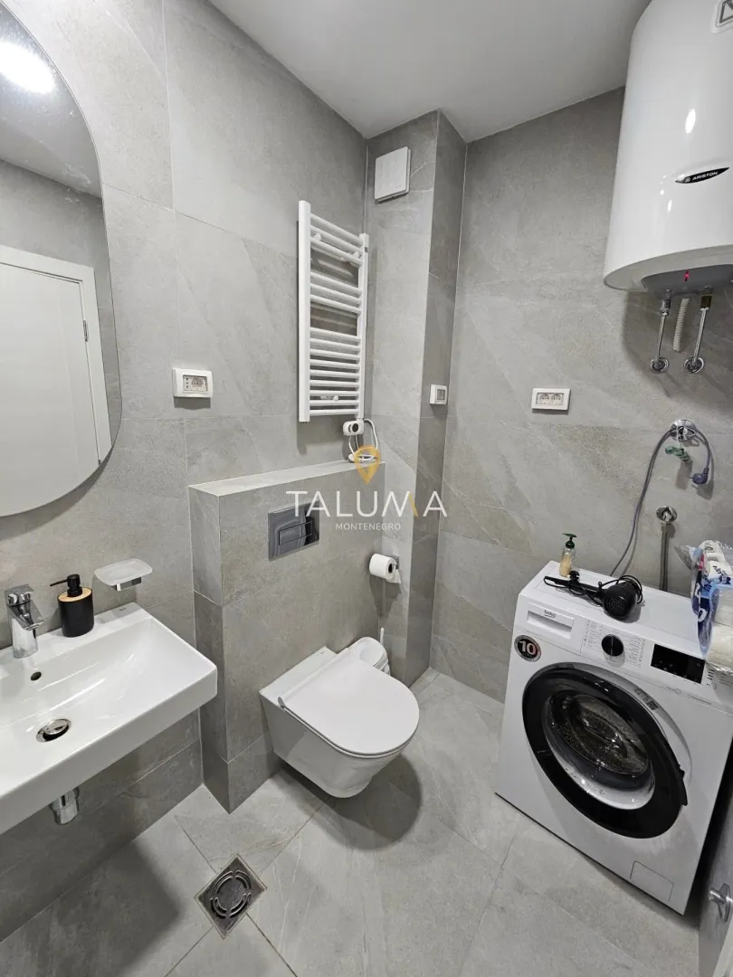 Modern bathroom with a sink, toilet, washing machine, and tiled walls.