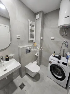Modern bathroom with a sink, toilet, washing machine, and tiled walls. - image 8