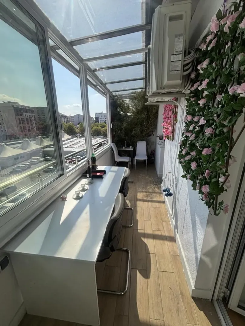 Glazed balcony with a seating table and decorative flowers.