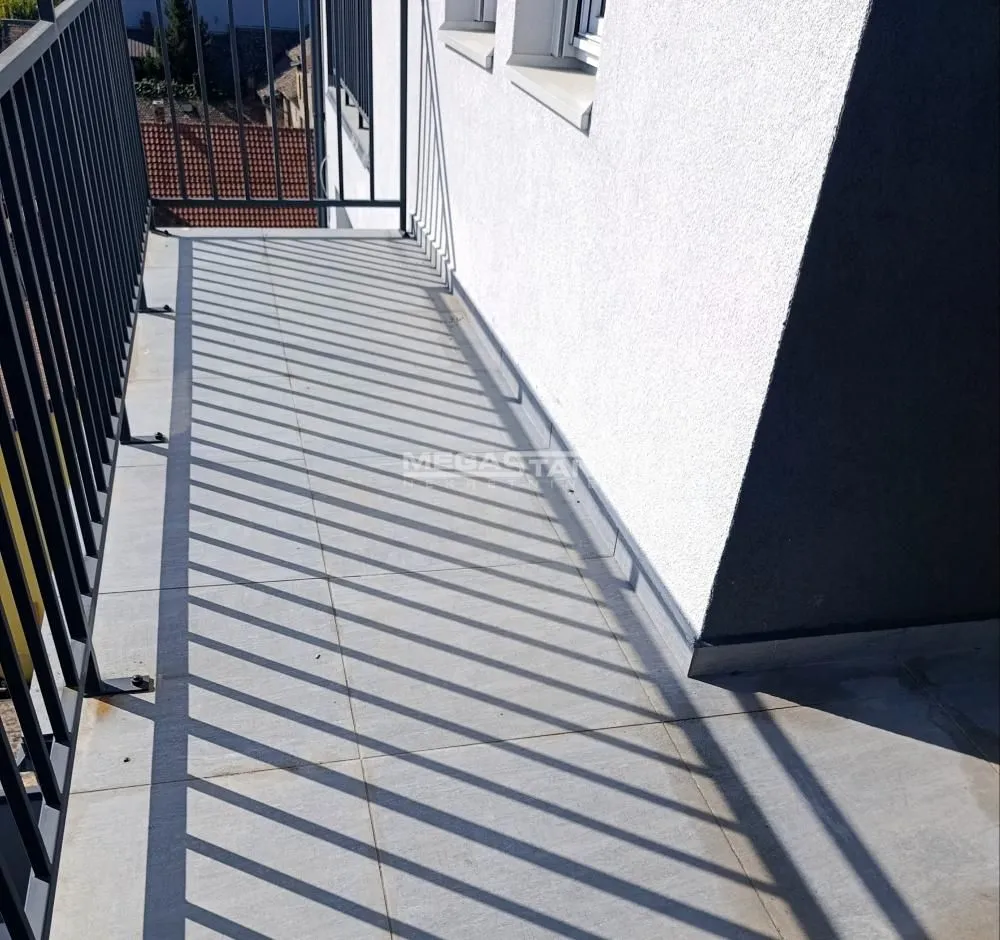 Dugačak popločani balkon sa crnom metalnom ogradom.