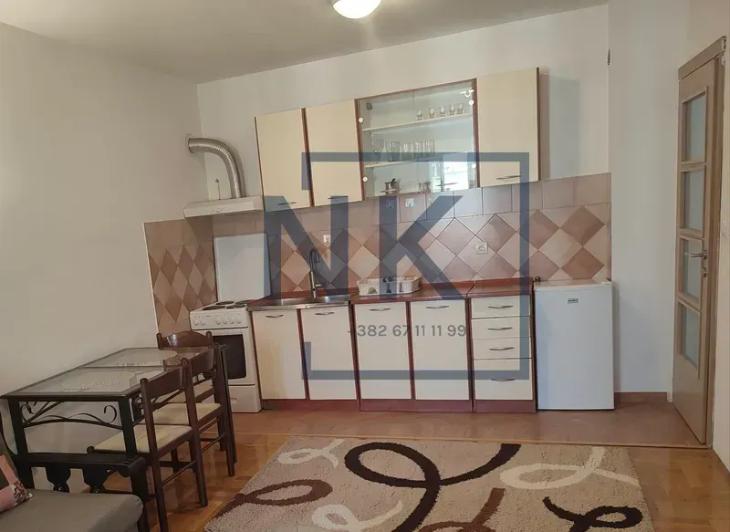 Manja kuhinja sa elementima, trpezarijskim stolom i frižiderom.