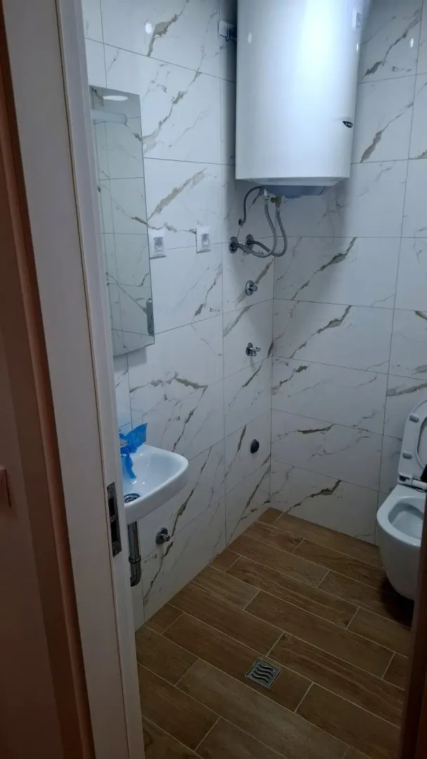 Pogled na kupatilo sa tuš kabinom, umivaonikom i bojlerom.