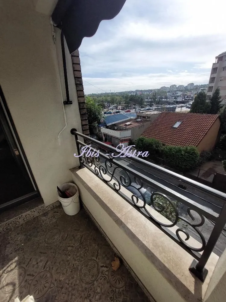Natkriveni balkon sa metalnom ogradom i pogledom na okolinu.