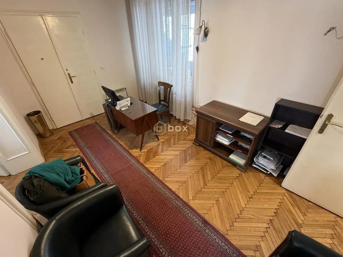 Dnevna soba sa radnim stolom, drvenim podom i kožnim foteljama.