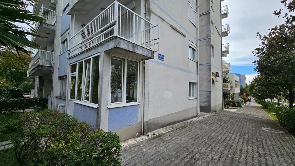 Eksterijer stambene zgrade sa balkonom i popločanim prolazom.