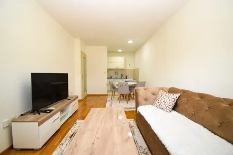 Living room with a sofa, television, and a view of the dining area and kitchen. - image 4