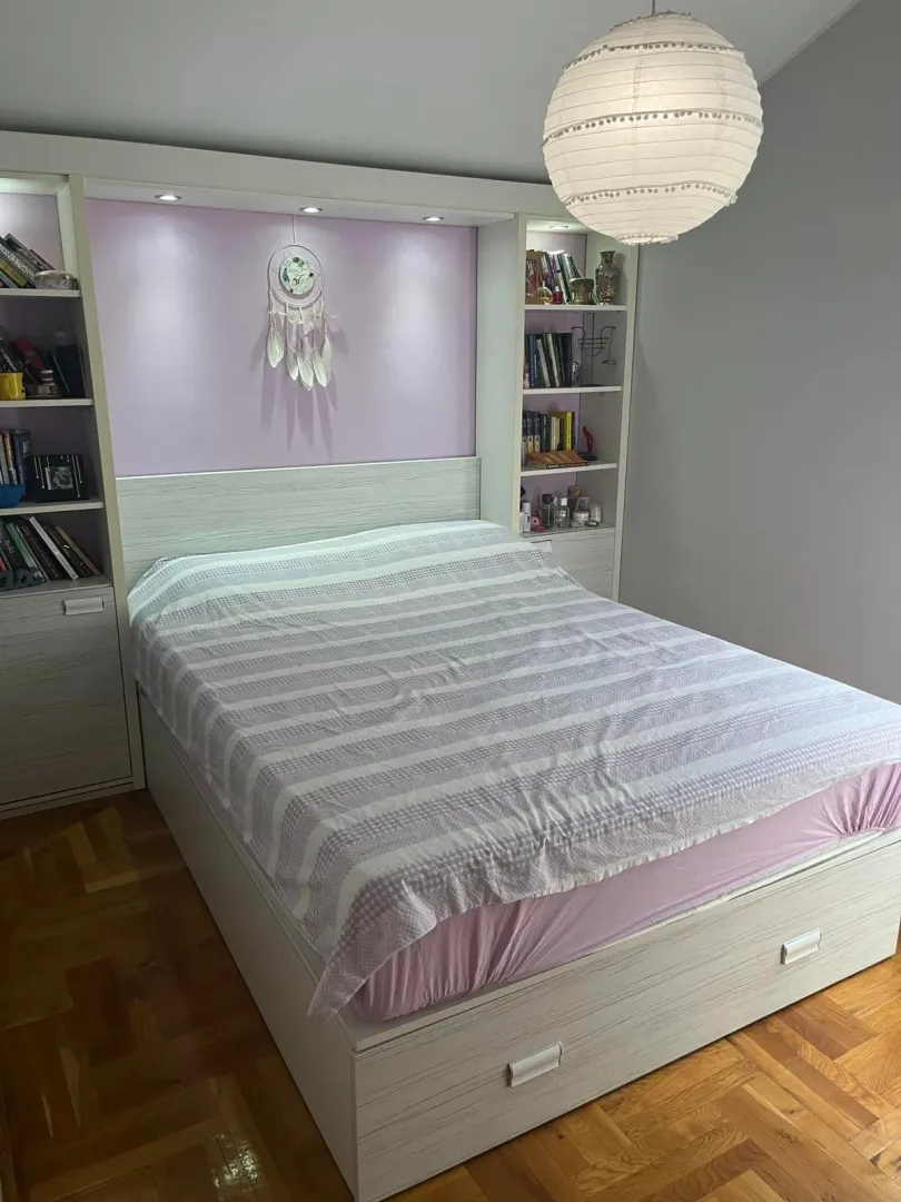 Furnished bedroom with a double bed, built-in shelves, and parquet flooring.