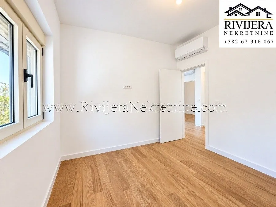 Empty room with white walls, wooden flooring, and an air conditioning unit.