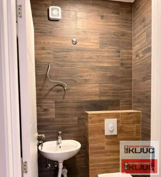 Manje kupatilo sa umivaonikom, WC šoljom i zidnim pločicama u dezenu drveta. - image 5