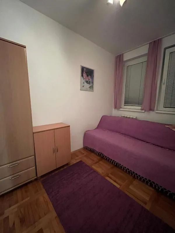 Manja spavaća soba sa krevetom, ormarom i drvenim podom.