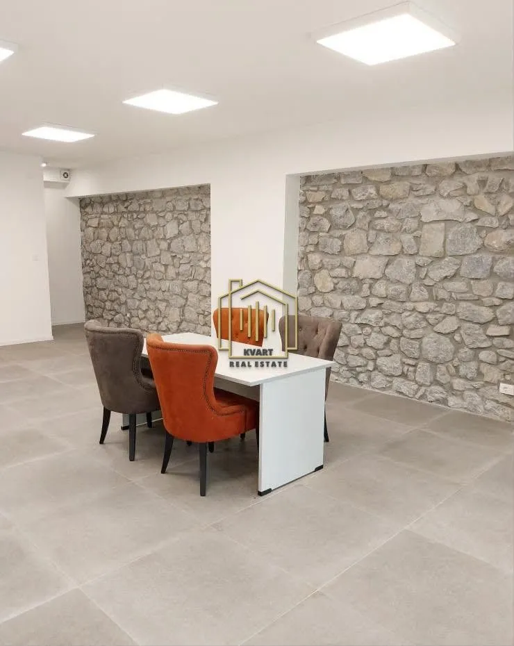 Dining table with chairs in a spacious room featuring a decorative stone wall.