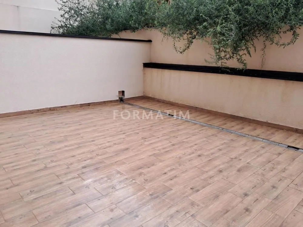 Tiled terrace with a wall and greenery in the background.
