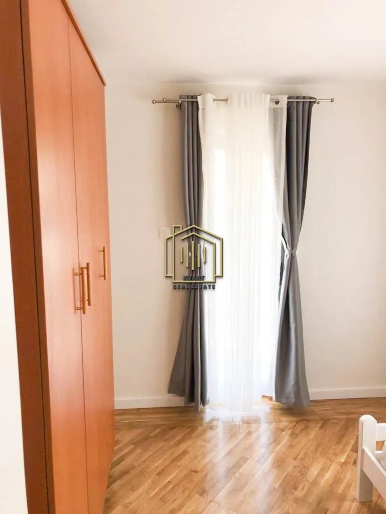 Spavaća soba sa drvenim podom, garderoberom i prozorom sa zavjesama.