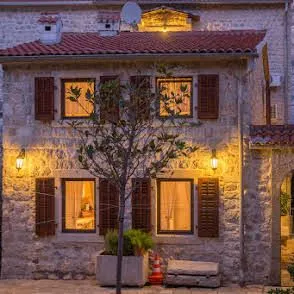 Pogled na fasadu tradicionalne kamene kuće sa osvijetljenim prozorima i drvenim šalukatima noću.