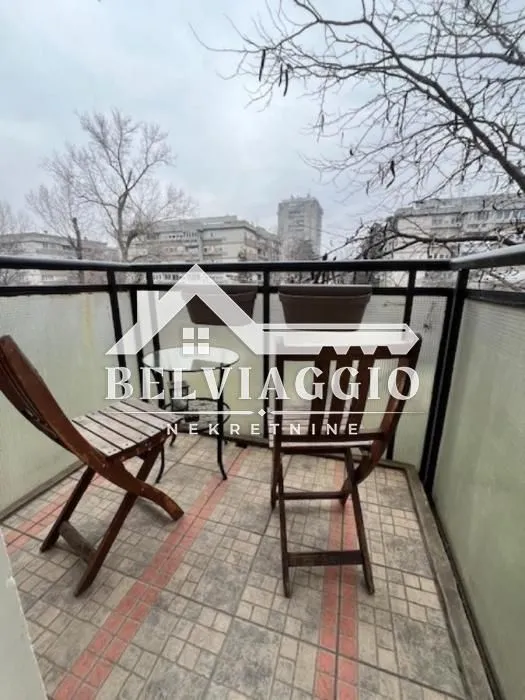Manji namješteni balkon sa stolom i dvije stolice i pogledom na grad.