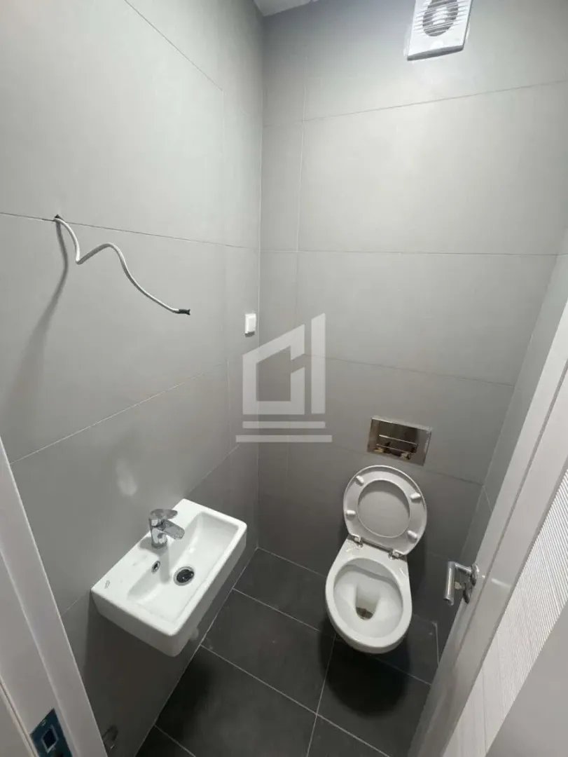 Manje kupatilo sa umivaonikom i šoljom obloženo sivim pločicama.