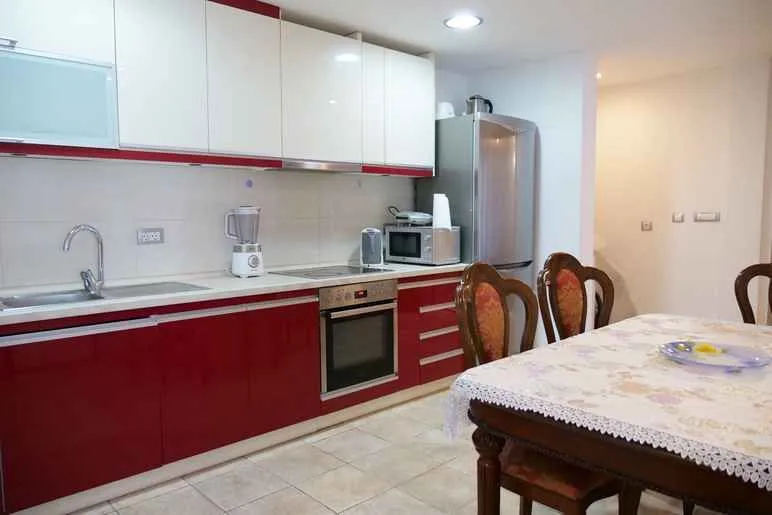 Kuhinja opremljena bijelim i crvenim elementima sa trpezarijskim stolom u prvom planu.