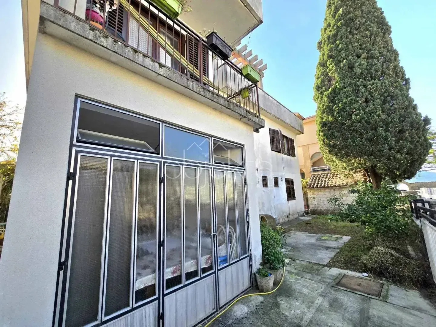 Pogled na dvorište i fasadu kuće sa balkonom.