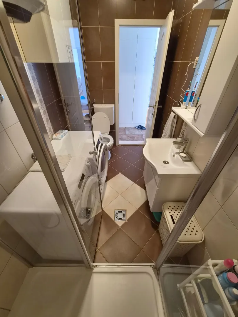 Manje kupatilo sa tuš kabinom, umivaonikom, veš mašinom i toaletom.