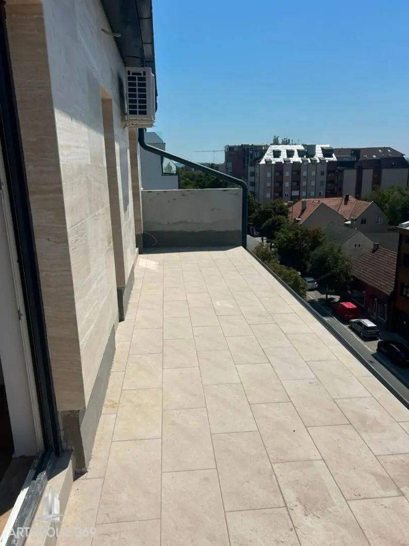 Prostrana popločana terasa sa pogledom na okolne zgrade i ulicu.