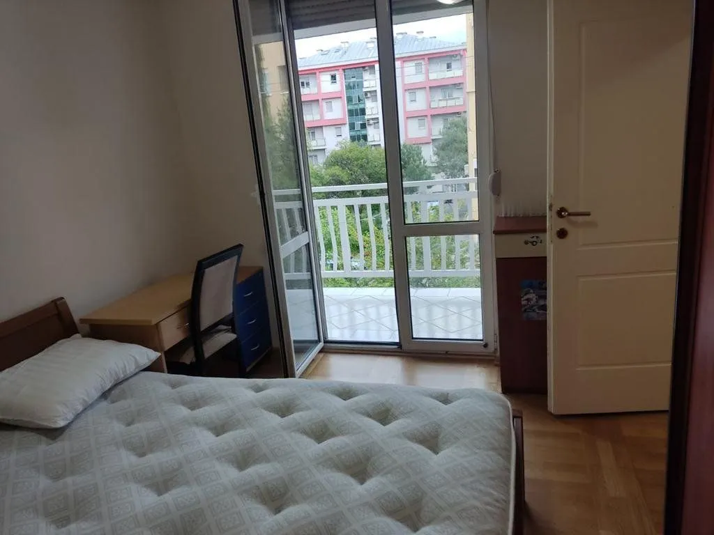 Namještena spavaća soba sa krevetom, radnim stolom i izlazom na terasu.