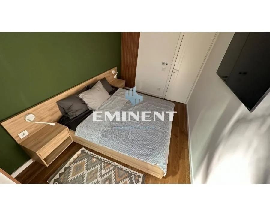 Furnished bedroom with a double bed, bedside tables, and a green accent wall.