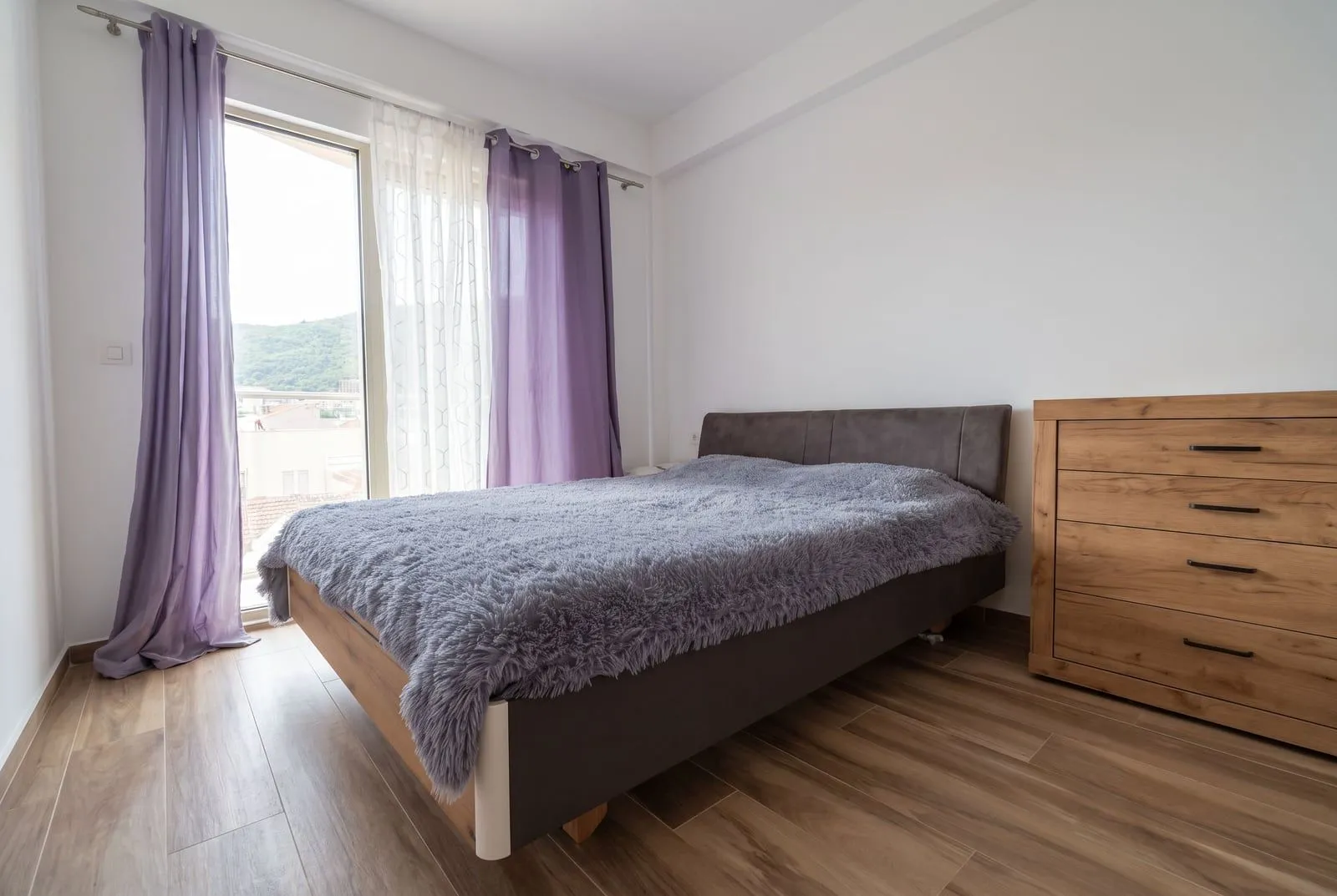 Bright bedroom with a double bed, wooden dresser, and balcony access.