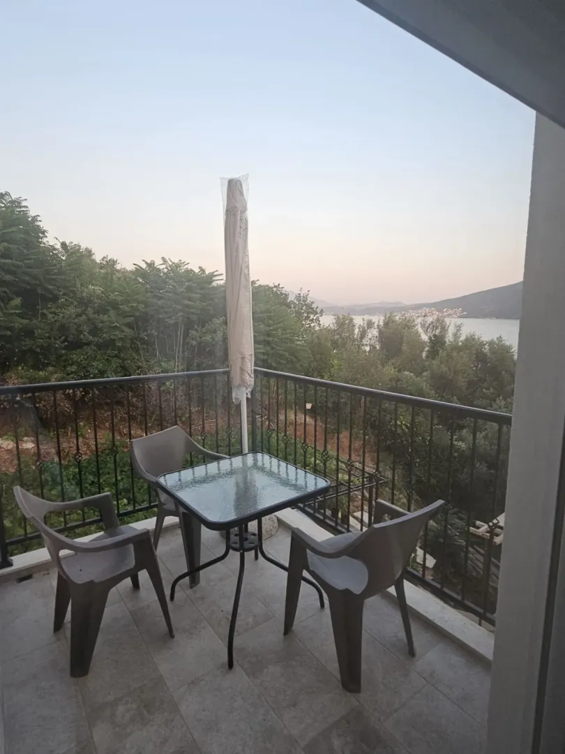 Namještena terasa sa stolom, stolicama i suncobranom, sa pogledom na more i zelenilo.