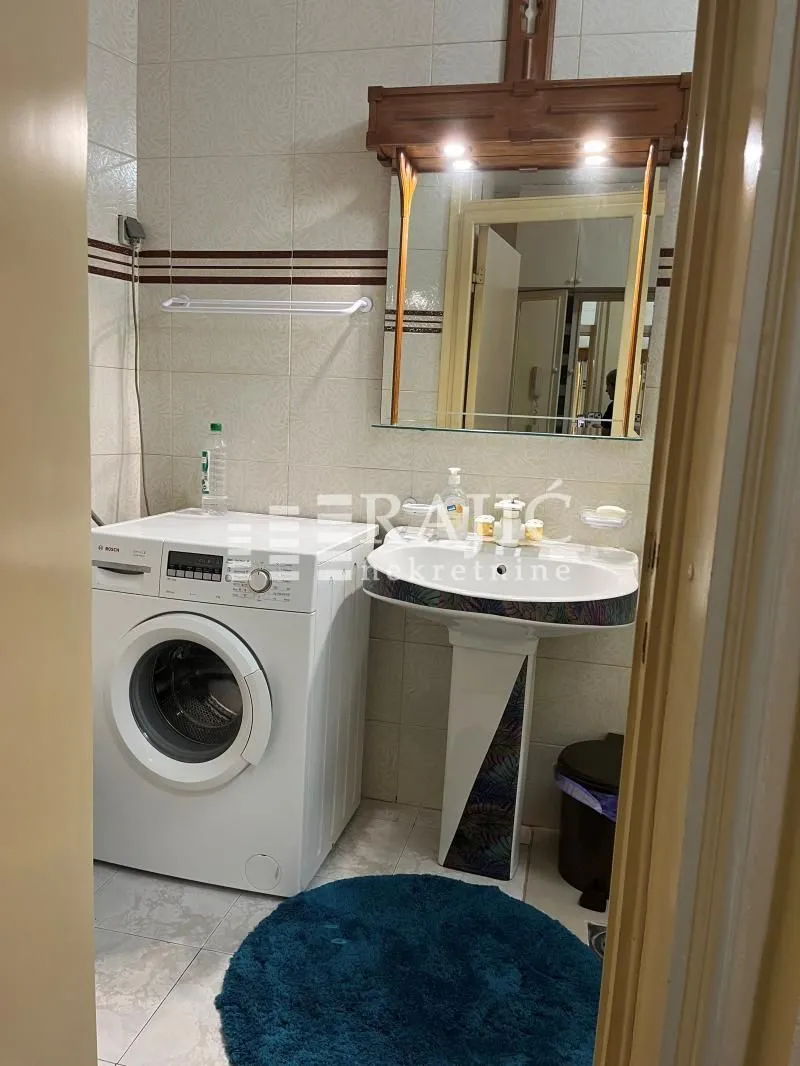 Smaller bathroom with a sink, mirror, washing machine and tiling.