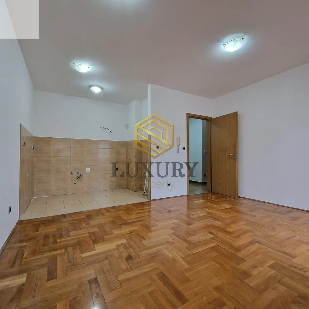 Empty room with parquet flooring and a prepared kitchen area.