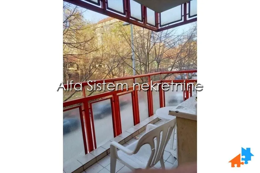 Natkriveni balkon sa pogledom na drveće i okolne zgrade.