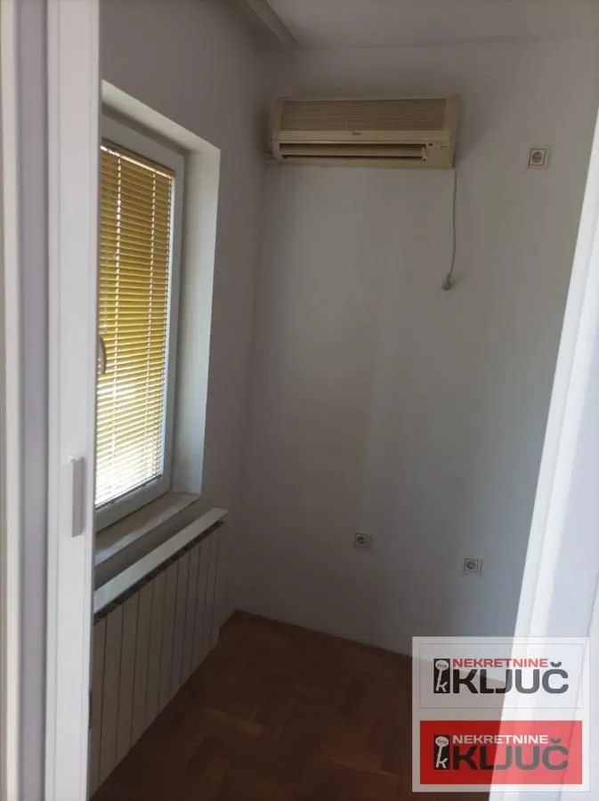 Manja prazna prostorija sa klima-uređajem i prozorom sa roletnama.