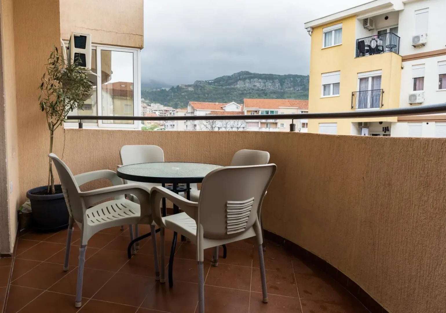 Furnished balcony with a table, chairs, and a view of surrounding buildings and hills.