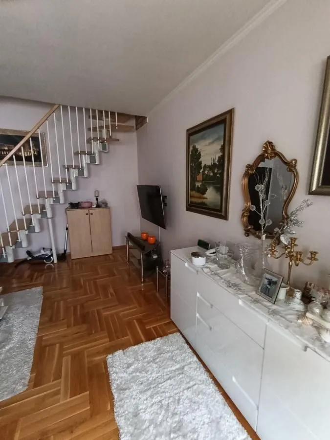Dnevna soba sa drvenim stepeništem i belom komodom.