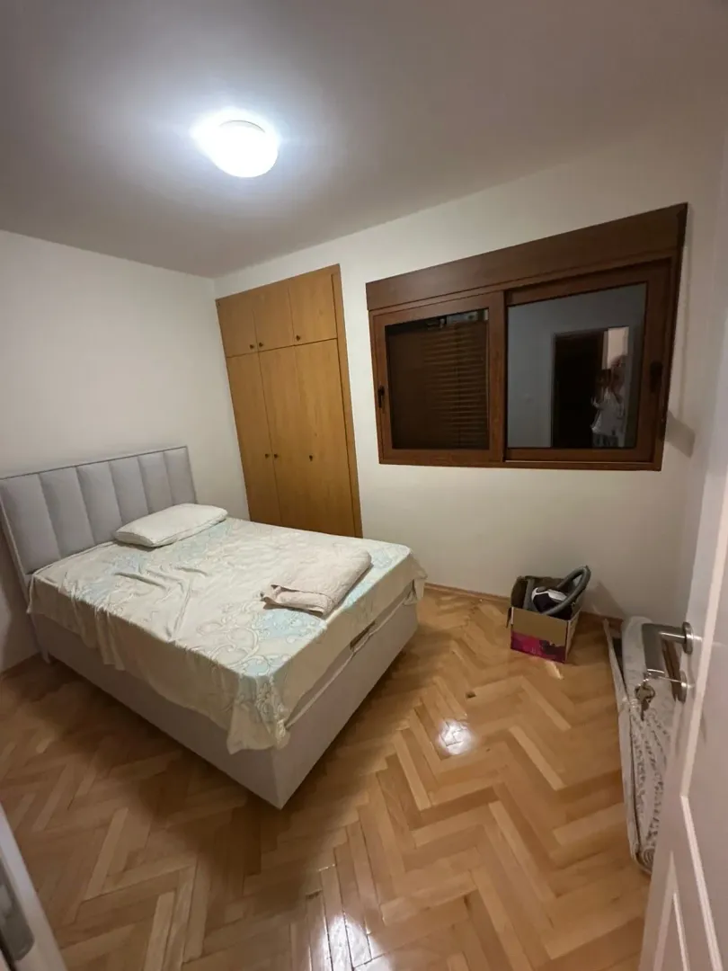 Manja spavaća soba sa bračnim krevetom, drvenim ormarom i parketom.