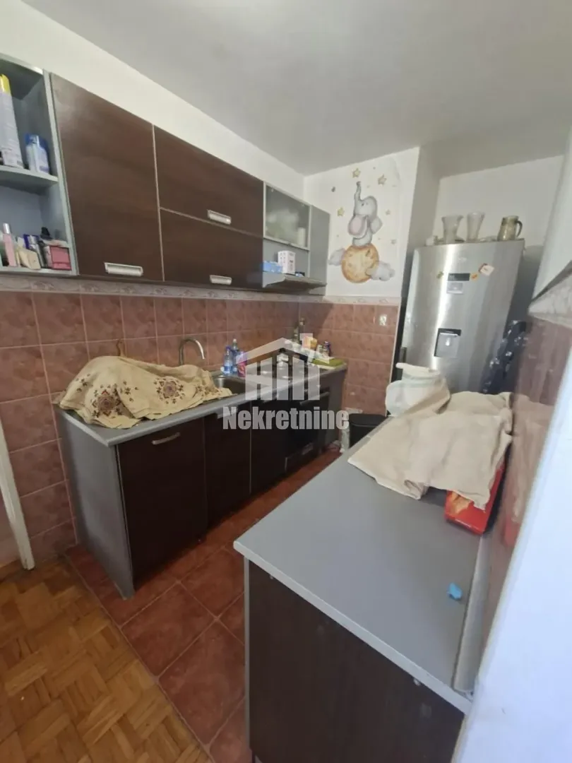 Manja kuhinja sa tamnim elementima i frižiderom.