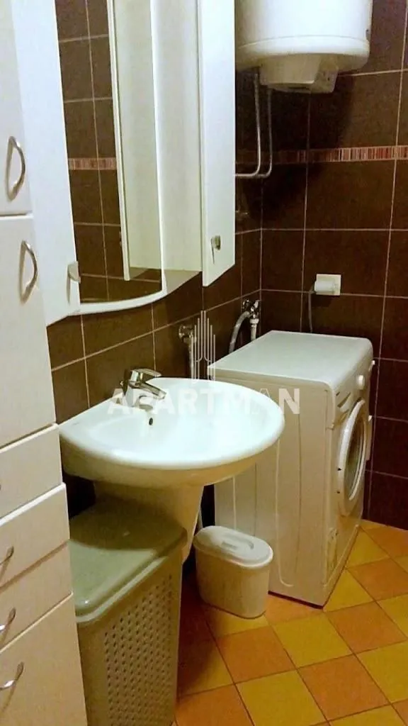 Bathroom with a washbasin, mirror, washing machine, and brown wall tiles.