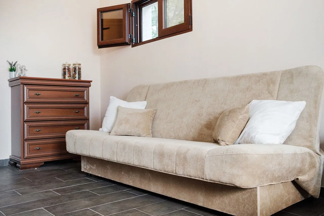 Living room with a beige sofa, wooden chest of drawers, and an open window.