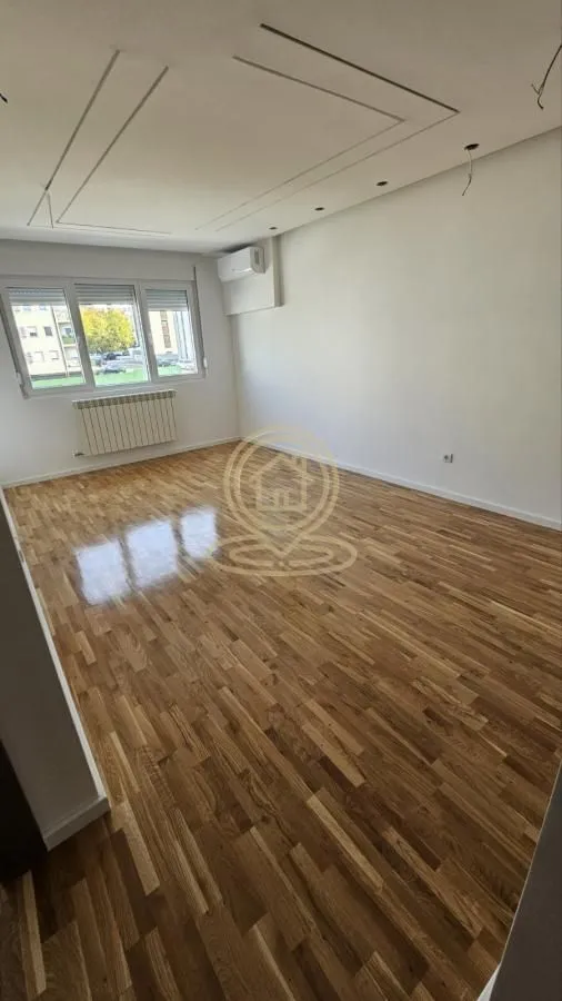 Prazna soba sa drvenim parketom i klima uređajem na zidu.