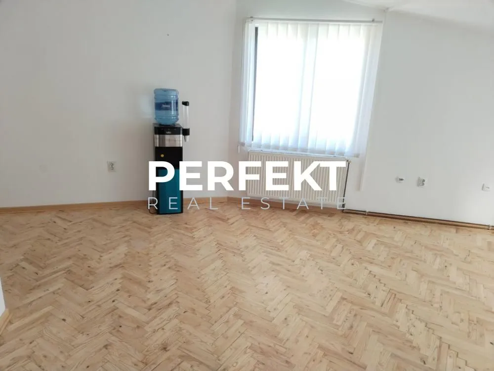 Empty room with hardwood parquet flooring and a water dispenser by the window.