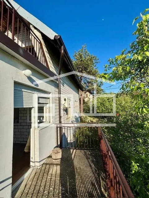 Balkon sa metalnom ogradom i pogledom na zelenilo.