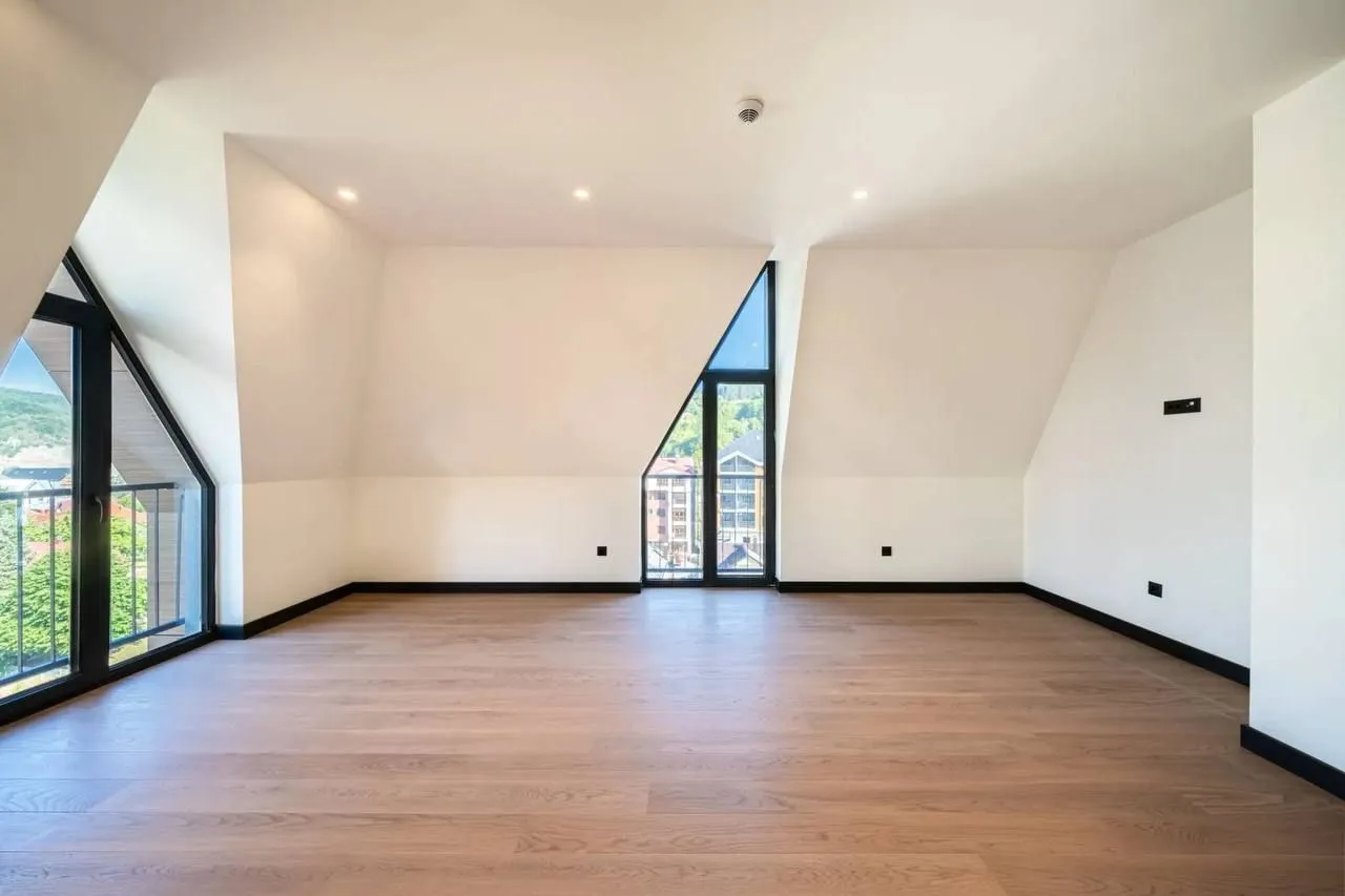 Spacious empty room with wooden flooring and large windows.