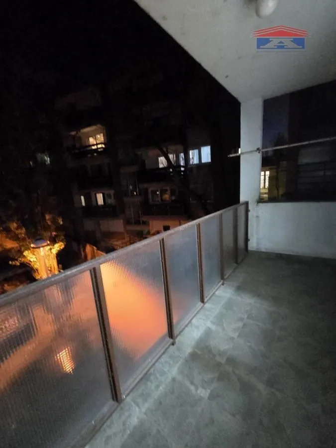Covered terrace with a metal railing and a view of surrounding buildings at night.