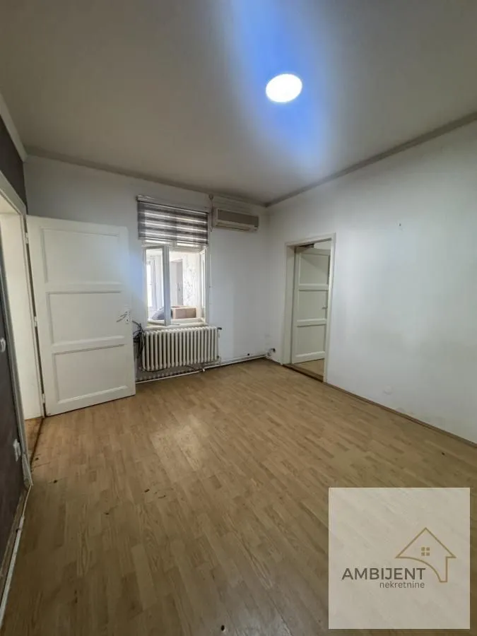 Prazna soba sa drvenim podom, belim zidovima i vratima.