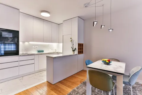 Modern white open-plan kitchen with a dining table and chairs. - image 6